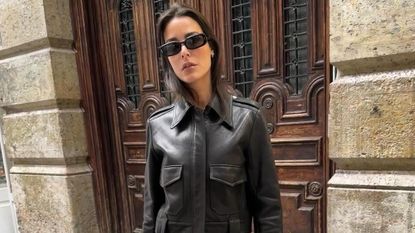 Influencer wearing brown leather jacket, black sunglasses, and black capri pants standing on Paris street.